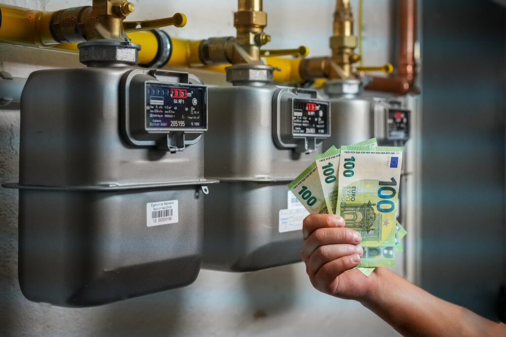 Person holding one hundred euro banknotes against gas meters - energy crisis in Europe concep